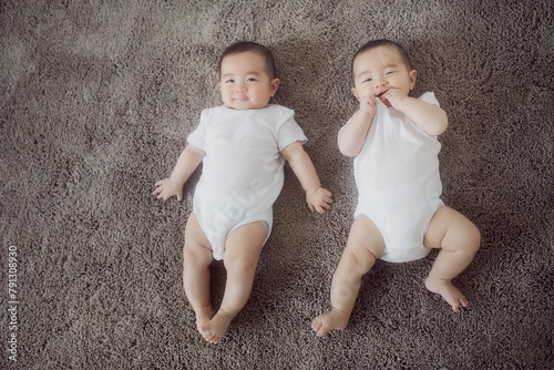 グレーのラグに寝転ぶ笑顔の双子の赤ちゃん photo