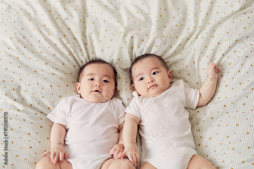 布団の上に寝転ぶ双子の赤ちゃん