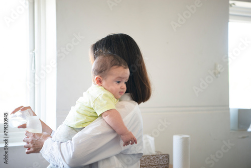 赤ちゃんを抱っこしながらミルクを作っている母親 photo