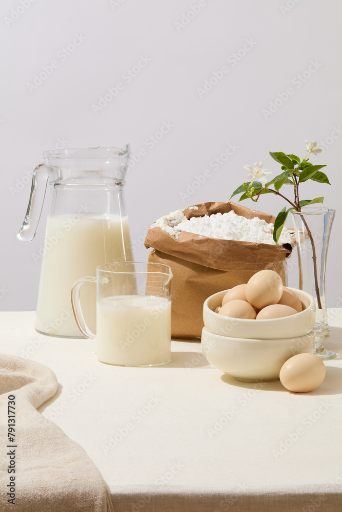 Front view of baking ingredients such as milk, a lot of eggs and a paper bag containing flour. A beautiful pot of flowers decorated. Empty space in the middle for product presentation Front view of baking ingredients such as milk, a lot of eggs and a paper bag containing flour. A beautiful pot of flowers decorated. Empty space in the middle for product presentation
