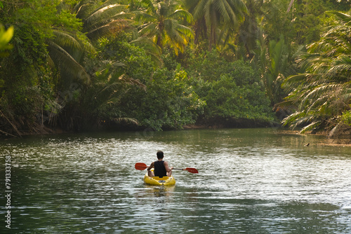 Asian traveller man kayaking on a muddy small river to see the mangrove forest, Thailand. There are many palm trees.(mangrove palm, nipa palm). Landscape travel and tourist concept..