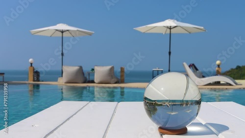 Closeup view of crystal ball on luxury infinity swimming pool with high sea view in sunny day. Blue cloudless sky. Deck chairs and umbrellas.