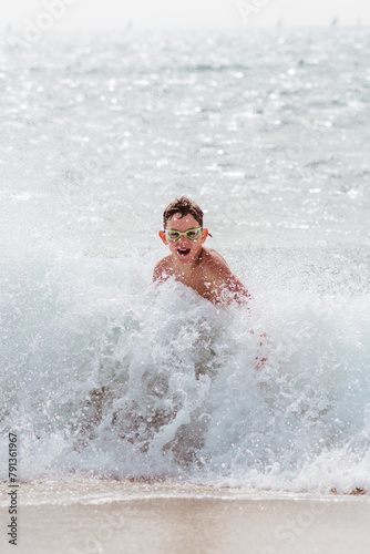 Young boy playing, running and splashing in strong sea waves. Smilling boy in swimsuit looking at waves. Concept of beach summer vacation with kids. © Halfpoint