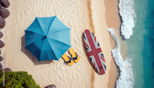 Aerial view of a sandy beach with ocean waves  featuring a beach umbrella and a United Kingdom flag-adorned surfboard in the sand. Embracing the United Kingdom leisure and tourism concept by the sea