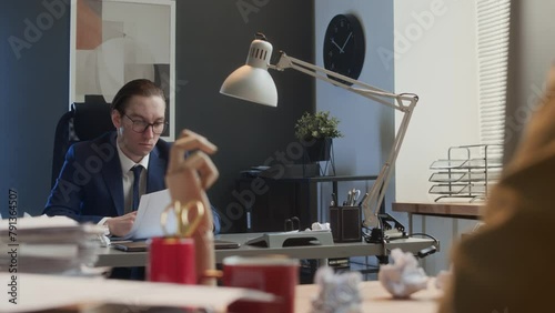 Medium over-shoulder shot of career man in suit and glasses working at desk in office, getting hit by crumpled paper from colleague, retaliating then engaging in vicious fightMedium over-shoulder shot photo