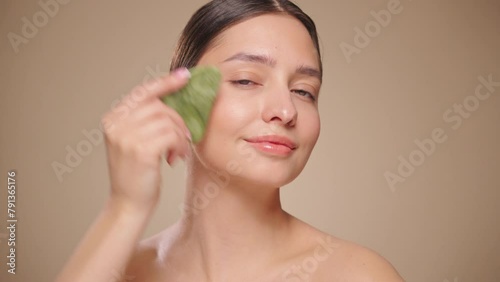 Beauty young woman doing skin care routine, scrapping, massage facial skin with jade gua sha scrapper, Facial treatment for anti aging and cosmetic cleaning. Slow motion