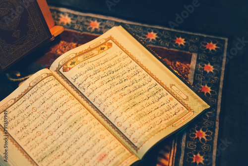 The Quran is opened for reading and placed on a prayer mat and has the golden glow of fire. Selective focus.
