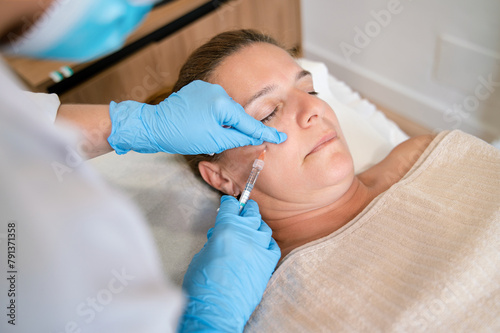 Faceless dermatologist administering facial cosmetic injection to woman