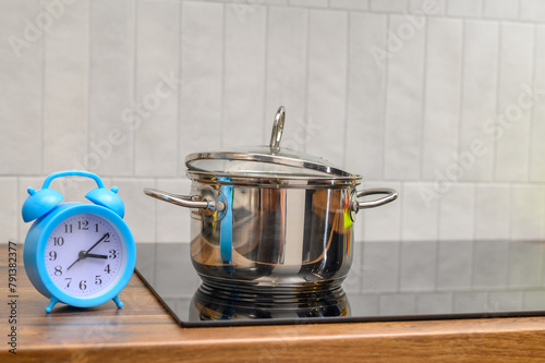 Czas gotowania, zegar stoi na blacie kuchennym obok stalowego garnka z gotującym się obiadem 