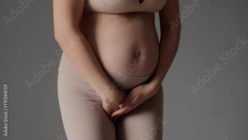 Constipation and belly cramps. Closeup of unrecognizable pregnant woman tummy female holding her bladder to pee isolated over gray background photo