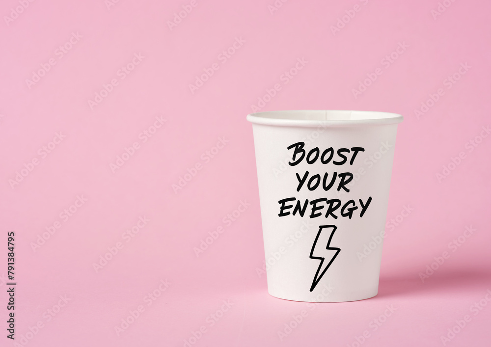 Boost your energy message on a paper coffee cup on pink background. Caffeine and energy boost concept. Boost your energy message on a paper coffee cup on pink background. Caffeine and energy boost concept.