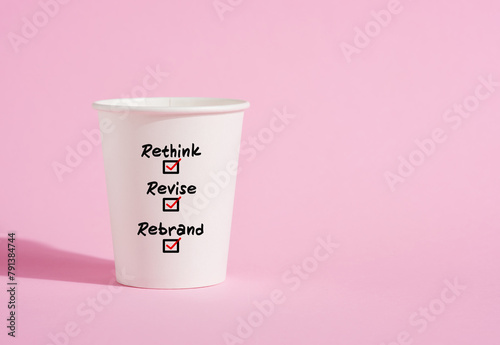 Rethink, revise and rebrand on a paper coffee cup on pink background. photo