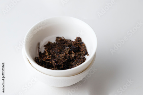 Dried tea leave s into the ceramic bowl on white background, tea time concept