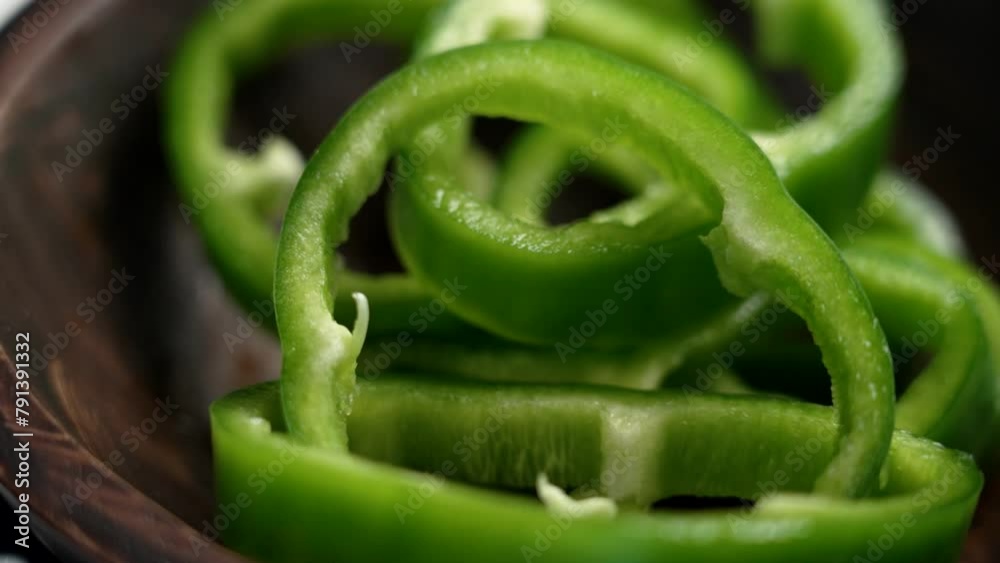 Organic green bell pepper slices falling into a brown rustic wooden bowl close up. Fresh vegetables. Slow motion Organic green bell pepper slices falling into a brown rustic wooden bowl close up. Fresh vegetables. Slow motion