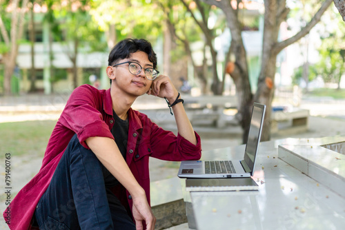 Portrait of Asian college student working with laptop  at the campus park. Asian man smiling and showing happy expression to camera