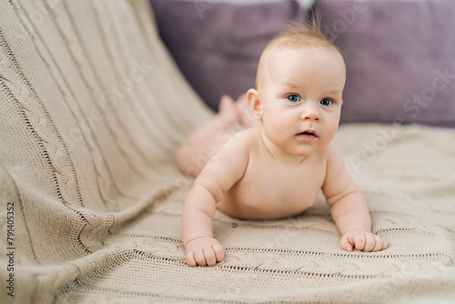 Portrait of cute little baby girl lying on stomach on bed, interestingly looking at camera with open mouth. Carefree healthy babyhood, healthcare and pediatrics care, purity, innocence concept. photo