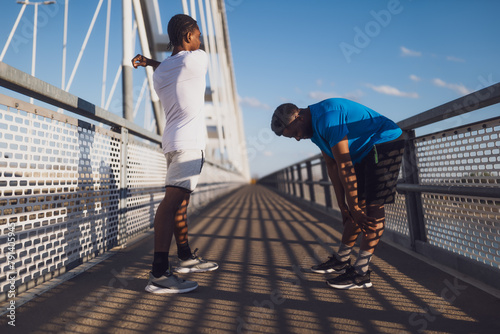 Two african-american friends are exercising on the bridge in the city. They are warming up for jogging. © djoronimo