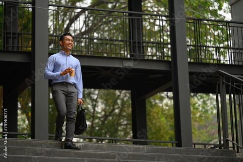 Confident smiling young businessman walking down the staircase outside his office