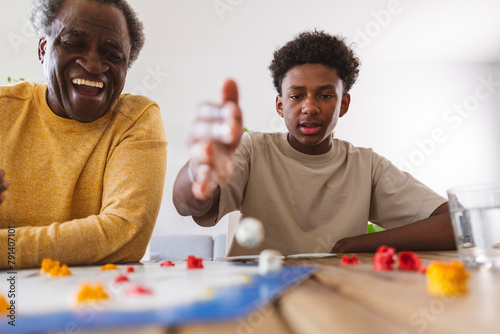 Happy senior man playing board game with grandson at home photo
