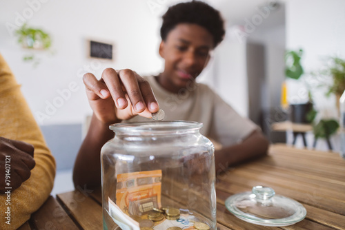 Teenage boy putting coin in savings jar by grandfather at home photo
