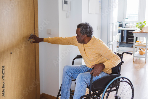 Senior man in wheelchair opening door at home photo