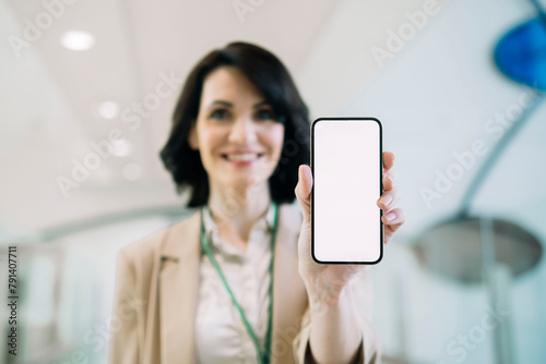 Smiling businesswoman showing smart phone with blank screen at office