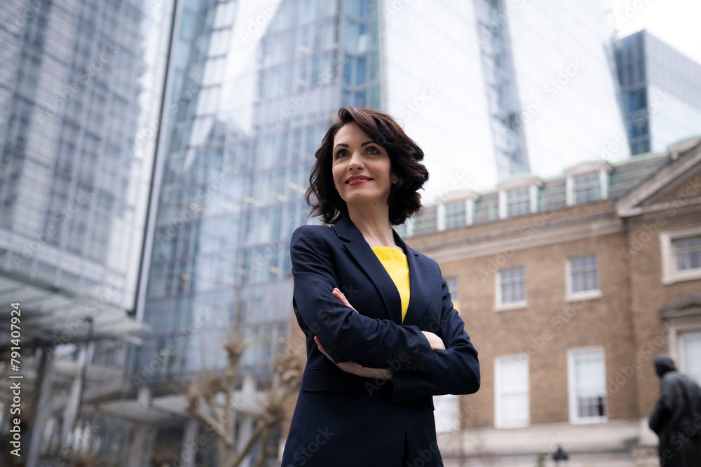 Smiling businesswoman in blazer standing with arms crossed Smiling businesswoman in blazer standing with arms crossed