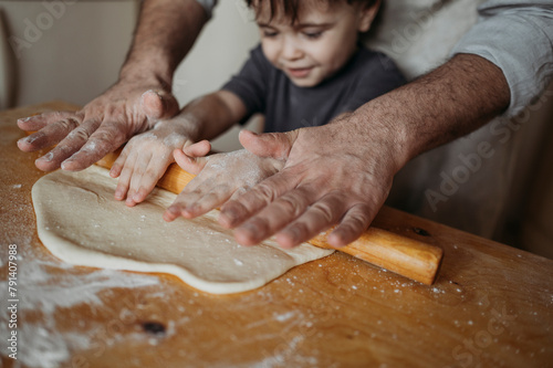 Father teaching son to roll dough in kitchen at home photo