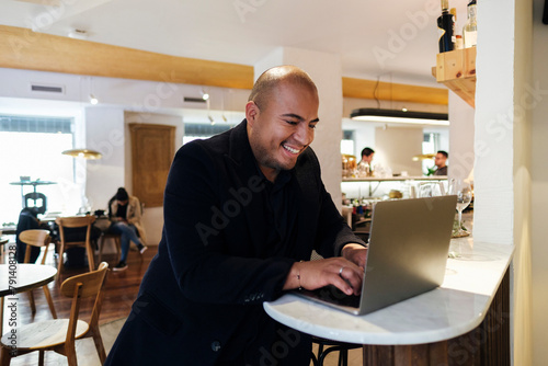 Smiling customer using laptop sitting at illuminated table in restaurant photo