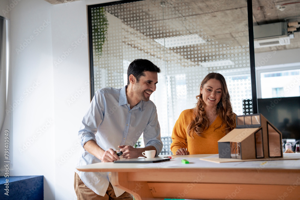 Smiling mature architects discussing over model home at desk Smiling mature architects discussing over model home at desk