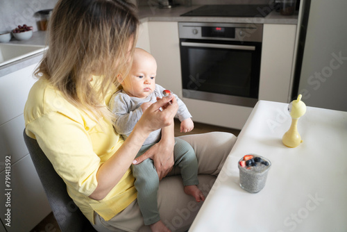 Blond mother feeding baby with yogurt in kitchen photo