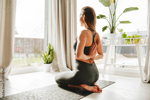 Woman doing reverse prayer pose on yoga mat at home photo