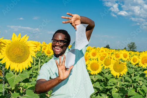 Carefree man tearing contract agreement amidst sunflowers in field photo