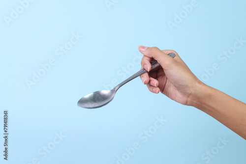 Canvas Print Woman's hand holds a stainless spoon on a blue pastel background.
