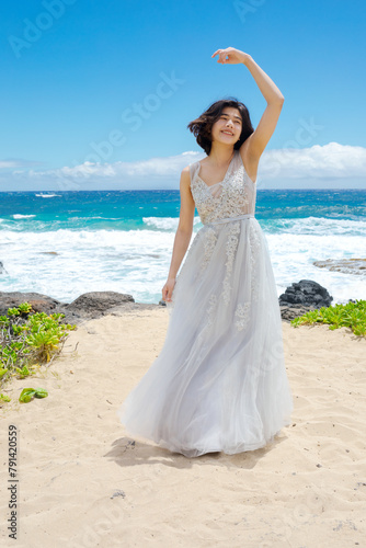 Teen girl in white dress twirling on Hawaiian beach