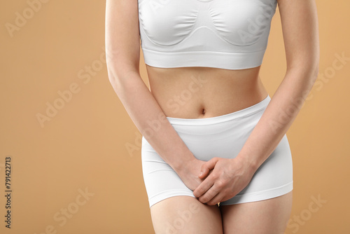 Woman suffering from cystitis on beige background, closeup. Space for text