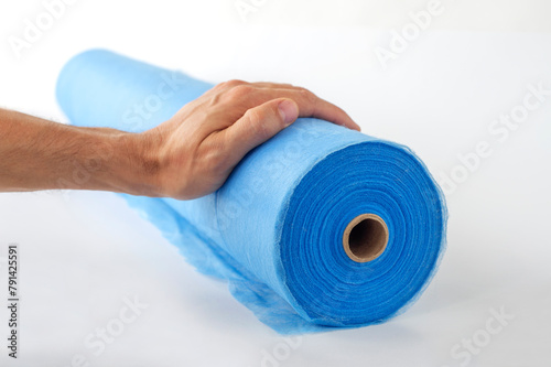 A hand unwinds a roll of blue fabric, a sheet for massage, on a white background.