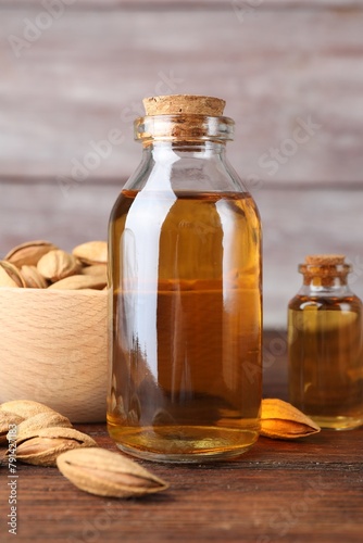 Almond oil in bottles and bowl with nuts on wooden table, closeup