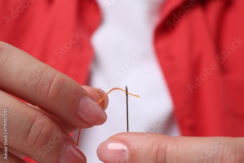 Woman inserting thread through eye of needle  closeup