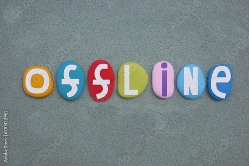 Offline, creative text composed with hand painted multi colored stone letters over green sand