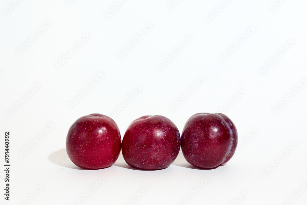 Three Fresh Red Plums Lined Up on a Bright White Background Three Fresh Red Plums Lined Up on a Bright White Background