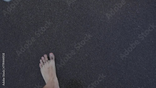 Cropped view of barefoot man walking on dark sand beach and go into sea. Above view on male feet in ocean water with waves photo