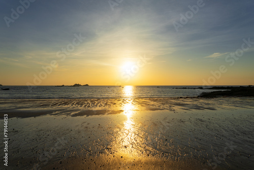 Coucher de soleil teintant le ciel de nuances de bleu et de jaune, illuminant le sable mouillé de reflets dorés sur la côte du Finistère nord en Bretagne. photo