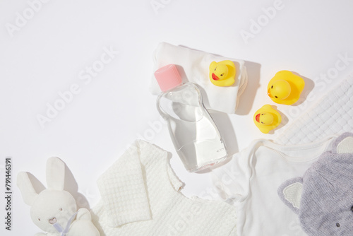Still life with baby hygiene and bath items  unlabeled shampoo bottle  different size rubber duck  bath towel and some clothes flat lay on white background. Blank space for advertising  top view