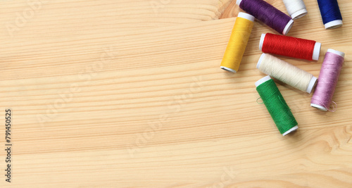 Spools of thread of different colors, top view. Set of various colorful sewing threads on a wooden table, close-up. Sewing