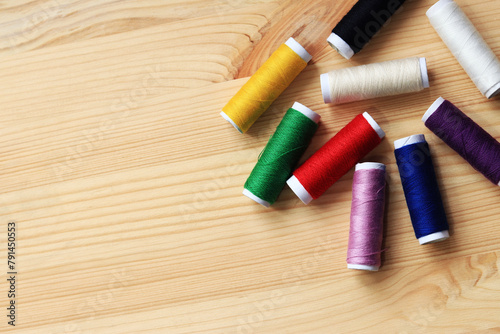 Spools of thread of different colors, top view. Set of various colorful sewing threads on a wooden table, close-up. Sewing