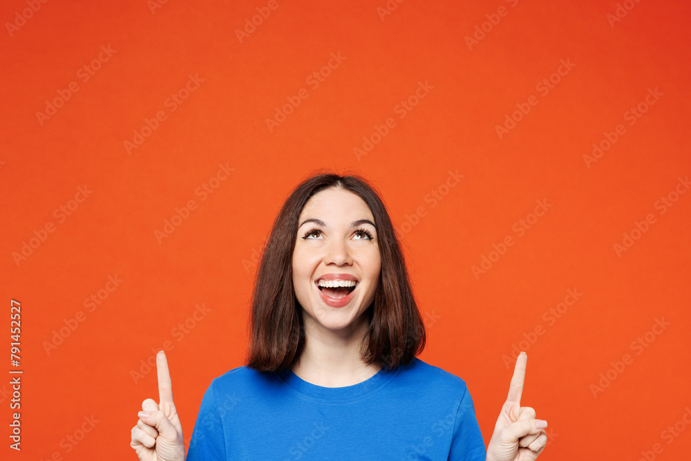 Young smiling happy cheerful woman wear blue t-shirt casual clothes point index finger overhead on area copy space mock up isolated on plain red orange background studio portrait. Lifestyle concept. - obrazy, fototapety, plakaty 