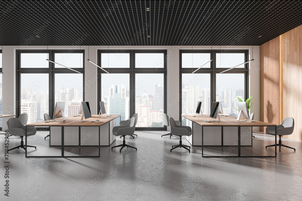 Obraz premium Stylish coworking interior with pc monitors on tables, panoramic window