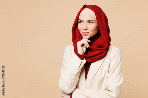 Young Arabian Asian Muslim woman wear abaya hijab suit clothes put hand prop up on chin, lost in thought and conjectures isolated on plain beige background. UAE middle eastern Islam religious concept.
