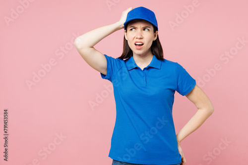 Professional delivery girl employee woman wear blue cap t-shirt uniform workwear work as dealer courier hold scratch head look aside isolated on plain pastel pink background studio. Service concept
